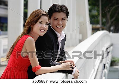 Stock Photo - Couple leaning over bridge railing, looking at camera. Fotosearch