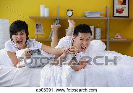 Couple lying on bed, playing video game View Large Photo Image Stock Image - Couple lying on bed, playing video game. Fotosearch