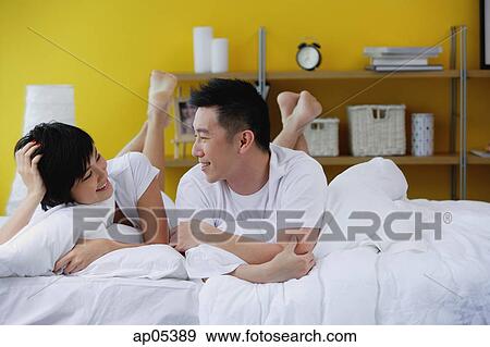 Stock Photo - Couple lying on bed, smiling at each other. Fotosearch