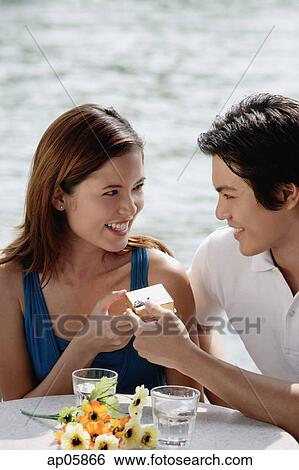 Stock Photograph - Couple sitting at outdoor cafe, man handing woman a gift box. Fotosearch