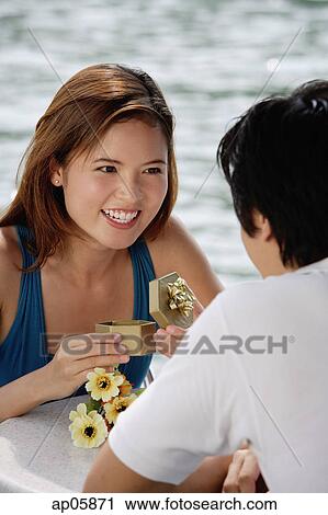 Couple sitting at outdoor cafe, woman opening gift box, smiling at man View Large Photo Image Stock Image - Couple sitting at outdoor cafe, woman opening gift box, smiling at man. Fotosearch