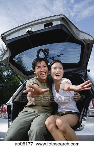 Couple sitting in boot of car, reaching towards camera View Large Photo Image Stock Photo - Couple sitting in boot of car, reaching towards camera. Fotosearch