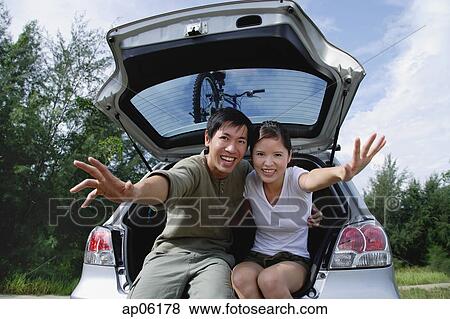 Couple sitting in boot of car, reaching towards camera, smiling View Large Photo Image Stock Photo - Couple sitting in boot of car, reaching towards camera, smiling. Fotosearch