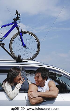 Stock Photo - Couple sitting in car, bicycle on the roof. Fotosearch