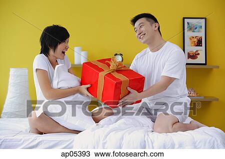Couple sitting on bed, man giving woman present View Large Photo Image Stock Image - Couple sitting on bed, man giving woman present. Fotosearch