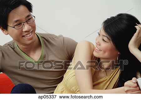 Couple sitting side by side, looking at each other View Large Photo Image Stock Photo - Couple sitting side by side, looking at each other. Fotosearch