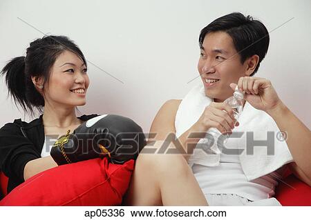 Stock Photograph - Couple sitting side by side, woman with boxing gloves, man holding bottled water. Fotosearch
