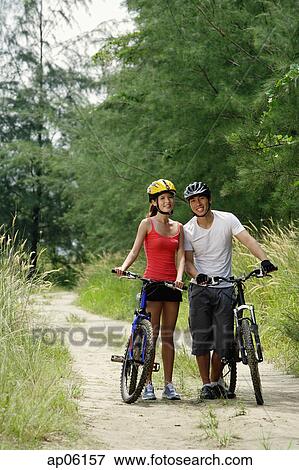 Couple standing with bicycles, smiling at camera View Large Photo Image Stock Photo - Couple standing with bicycles, smiling at camera. Fotosearch