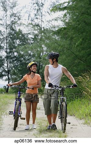 Stock Photograph - Couple walking with bicycles, looking at each other. Fotosearch