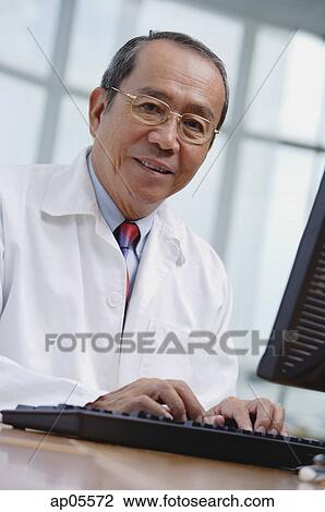 Doctor in office, using desktop computer, looking at camera View Large Photo Image Stock Image - Doctor in office, using desktop computer, looking at camera. Fotosearch