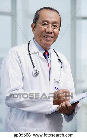 Doctor writing on medical chart, looking at camera View Large Photo Image Stock Photo - Doctor writing on medical chart, looking at camera. Fotosearch