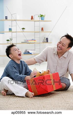 Father and son at home, boy opening gift, looking up View Large Photo Image Stock Photography - Father and son at home, boy opening gift, looking up. Fotosearch