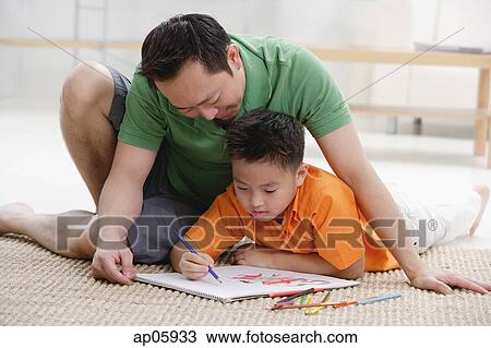 Stock Image - Father and son at home, drawing on sketchbook. Fotosearch