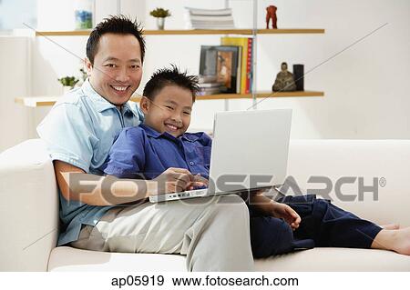 Father and son in living room with laptop, smiling at camera View Large Photo Image Stock Photo - Father and son in living room with laptop, smiling at camera. Fotosearch