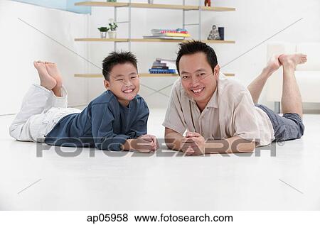 Father and son lying on floor, smiling at camera, portrait View Large Photo Image Stock Photo - Father and son lying on floor, smiling at camera, portrait. Fotosearch