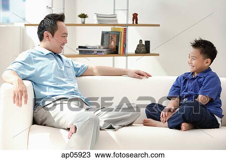 Father and son sitting on sofa, smiling at each other View Large Photo Image Stock Image - Father and son sitting on sofa, smiling at each other. Fotosearch
