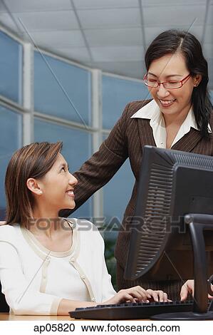 Female executive at computer, smiling at woman standing next to her View Large Photo Image Stock Image - Female executive at computer, smiling at woman standing next to her. Fotosearch