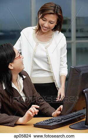 Picture - Female executive at desk smiling at woman standing next to her. Fotosearch