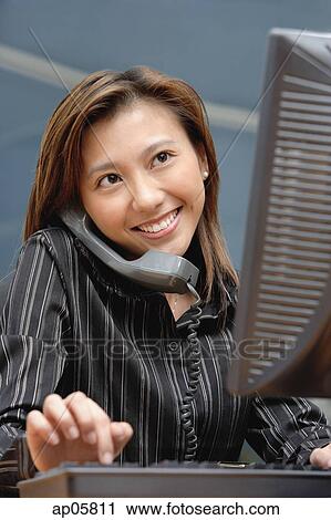 Female executive at desk, using computer and telephone, smiling View Large Photo Image Stock Image - Female executive at desk, using computer and telephone, smiling. Fotosearch
