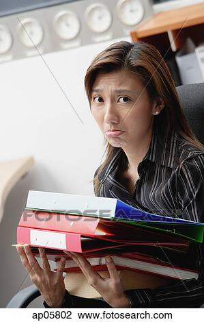 Stock Image - Female executive carrying folders and binders, frowning. Fotosearch