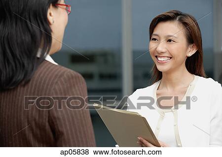 Stock Photo - Female executive handing folders over to woman in front of her. Fotosearch