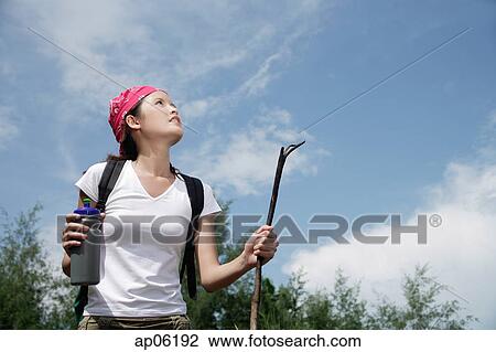 Stock Image - Female hiker looking up, low angle view. Fotosearch