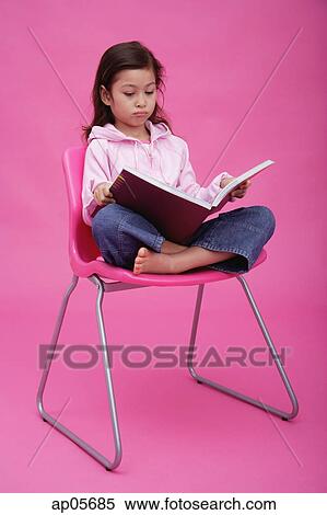 Stock Photography - Girl on chair, reading a book, frowning. Fotosearch