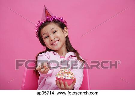 Girl wearing party hat, holding bowl of cake towards camera View Large Photo Image Picture - Girl wearing party hat, holding bowl of cake towards camera. Fotosearch