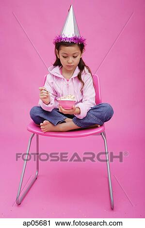 Girl with party hat, sitting on chair, holding bowl of cake View Large Photo Image Stock Image - Girl with party hat, sitting on chair, holding bowl of cake. Fotosearch