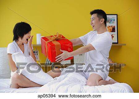 Picture - Man giving woman present in bedroom. Fotosearch