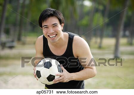 Stock Image - Man holding soccer ball, smiling. Fotosearch
