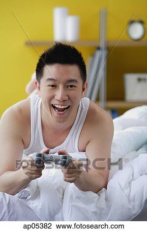 Man lying on bed, playing video game View Large Photo Image Stock Image - Man lying on bed, playing video game. Fotosearch