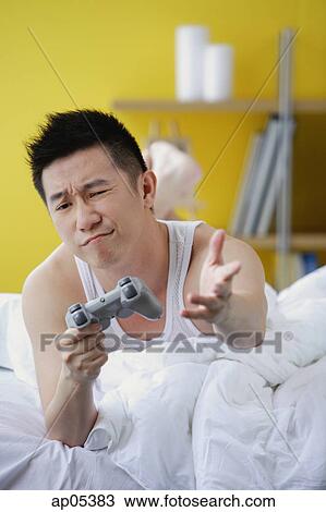 Man lying on bed, playing video game, making a face View Large Photo Image Stock Image - Man lying on bed, playing video game, making a face. Fotosearch