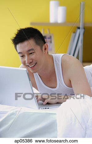 Man lying on bed using laptop View Large Photo Image Stock Photograph - Man lying on bed using laptop. Fotosearch
