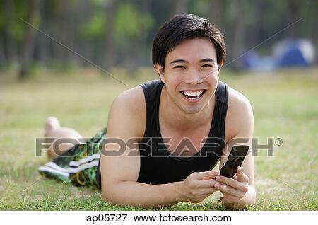 Man lying on grass, holding mobile phone View Large Photo Image Stock Photo - Man lying on grass, holding mobile phone. Fotosearch