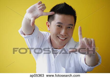 Stock Image - Man making finger frame, smiling at camera. Fotosearch
