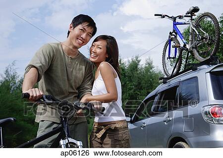 Stock Photograph - Man on a bike, woman standing next to him, looking at camera. Fotosearch
