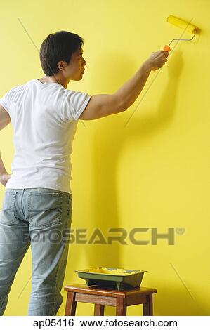Stock Photograph - Man painting wall with yellow paint. Fotosearch