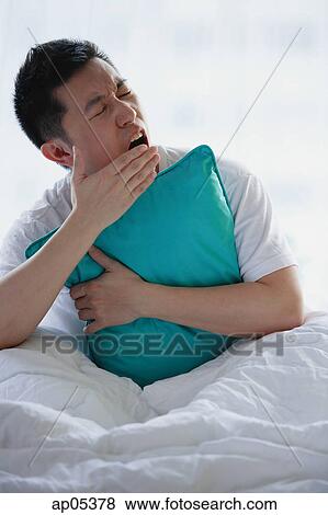 Man sitting in bed, embracing pillow, yawning View Large Photo Image Stock Photo - Man sitting in bed, embracing pillow, yawning. Fotosearch