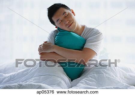Man sitting in bed, embracing pillow View Large Photo Image Stock Photograph - Man sitting in bed, embracing pillow. Fotosearch