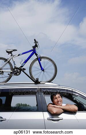 Stock Image - Man sitting in car, leaning out of window, bicycle on the roof of car. Fotosearch