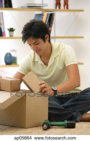 Picture - Man sitting on floor, looking through box. Fotosearch