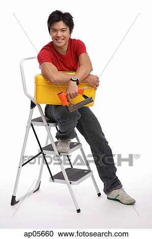 Stock Image - Man sitting on stepladder, holding toolbox and tools. Fotosearch