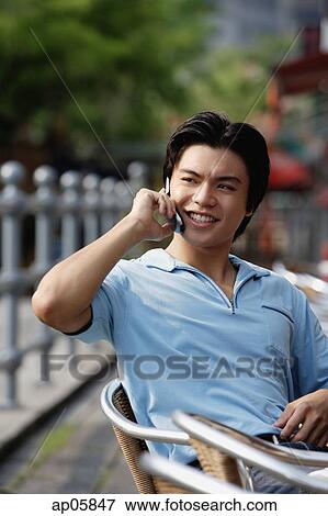 Stock Photo - Man sitting outdoors, using mobile phone. Fotosearch