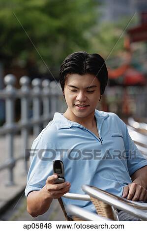 Stock Photo - Man sitting outdoors, using mobile phone, text messaging. Fotosearch