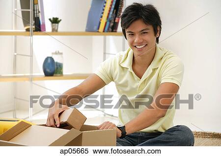 Stock Photography - Man sitting with box, smiling at camera. Fotosearch