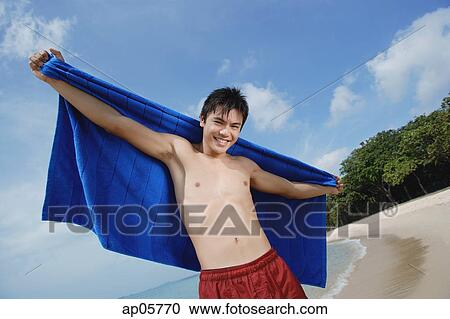 Man standing on beach, holding towel View Large Photo Image Stock Image - Man standing on beach, holding towel. Fotosearch