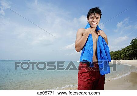Man standing on beach, holding towel around his neck View Large Photo Image Stock Image - Man standing on beach, holding towel around his neck. Fotosearch