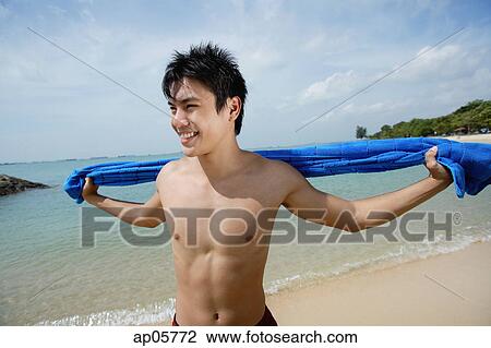 Man standing on beach, holding towel, looking away View Large Photo Image Stock Image - Man standing on beach, holding towel, looking away. Fotosearch