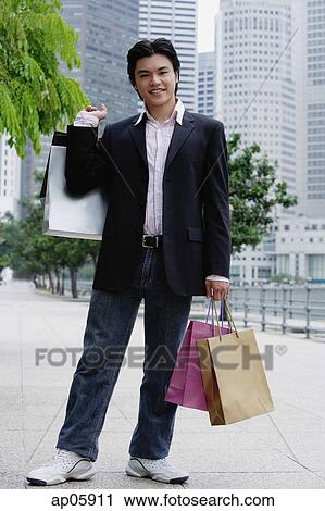 Man standing with shopping bags, smiling at camera View Large Photo Image Stock Image - Man standing with shopping bags, smiling at camera. Fotosearch